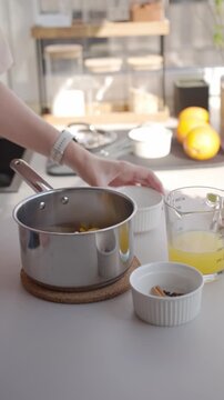 Hand adds sugar, orange juice and spices to saucepan for candied orange peel.