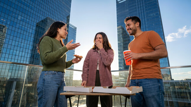Multiethnic friends sharing pizza on rooftop terrace above modern city skyline