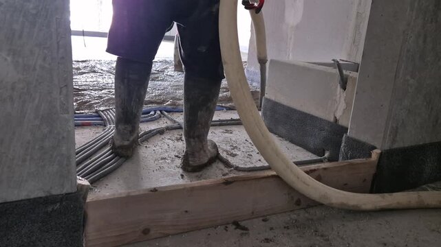 Construction workers pouring and measuring the thickness of lightweight polystyrene concrete insulation floor in a new apartment.