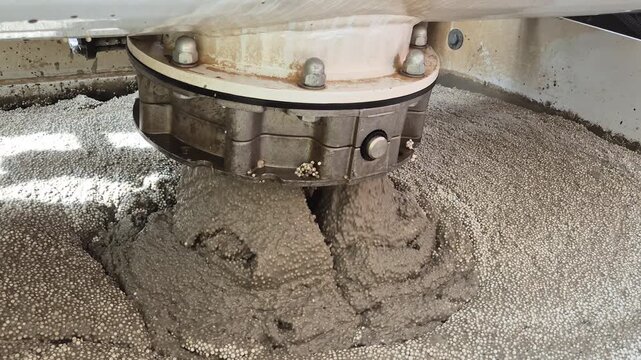 Close-up shot of lightweight polystyrene concrete pouring from the hopper into the mixer trough, showing detailed material structure.