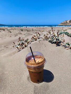 Frappe Cold refreshment iced coffee on a sandy beach. Freddo espresso refreshment at summertime. Beach umbrellas in a holiday resort. Frape.