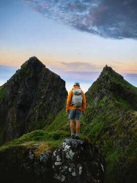 Man tourist standing alone in mountains travel in Norway climbing solo adventure summer vacations tour outdoors, hiker with backpack enjoying sunset Lofoten islands view freedom harmony with nature