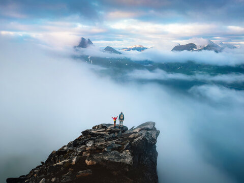 Family father and child climbing mountains standing on cliff edge enjoying foggy clouds view, hiking vacations in northern Norway parent and kid explore Senja outdoor active adventure tour together
