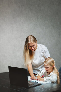 Mother helping her child girl writing homeschooling education studying in online school platform using laptop indoors, kid on distance learning family lifestyle modern technology and parent teaching
