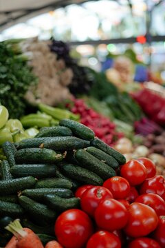 Vertical close-up of fresh organic cucumbers and ripe red tomatoes displayed at a market stall