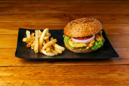 Appetizing gourmet burger with a sesame bun and onion rings served with a side of crispy french fries on a black plate