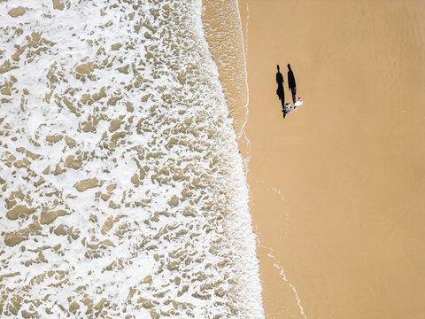 Top-Down Drone View of a Couple Walking as a Wave Washes Over the Beach