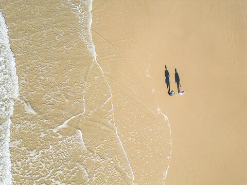 Top-Down Drone View of a Couple Walking as a Wave Washes Over the Beach