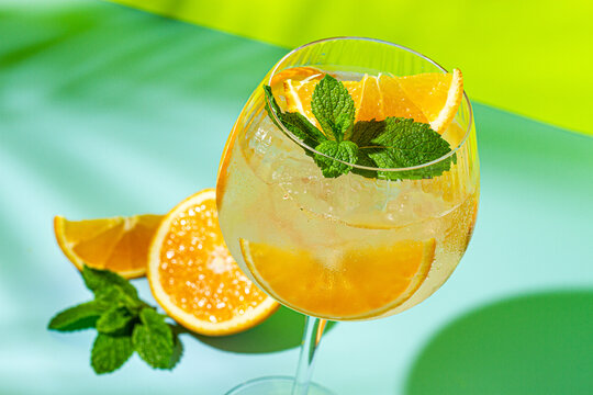 Refreshing drink is served in a glass with ice, mint, and orange slices in bright summer light