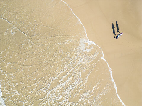 Top-Down Drone View of a Couple Walking as a Wave Washes Over the Beach