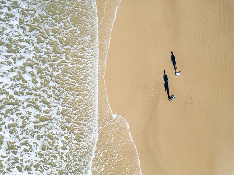 Top-Down Drone View of a Couple Walking as a Wave Washes Over the Beach