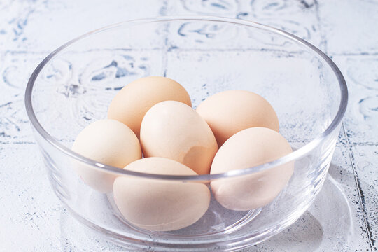 Fresh eggs in a clear glass bowl, ready to cook, natural light, no people,