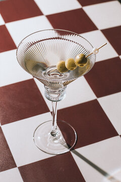 A martini glass with green olives, on a chessboard-style table, in the evening, vintage, retro, no people