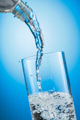 Clear drinking water pouring into a tall glass from a transparent plastic bottle.