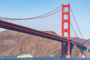 Ferry boat passes beneath the long and colorful span of Golden Gate Bridge