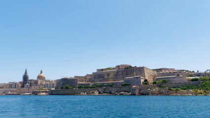 Naklejka premium Iconic city skyline with the famous church dome and massive stone bastions viewed from the sea at Grand Harbour, Valletta, Malta
