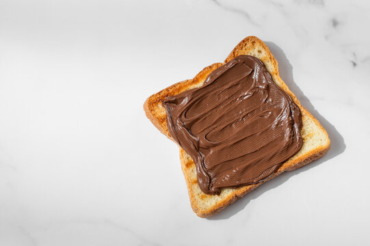Toasted bread with chocolate cream on a marble background close up.