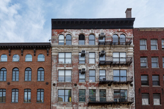 Pattern of fire escapes and window air conditioning units  on side of older brick building in New York City with blue sky above