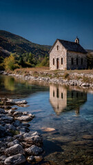 Fototapeta premium Historic Stone Church by River with Reflection in Clear Water Croatia