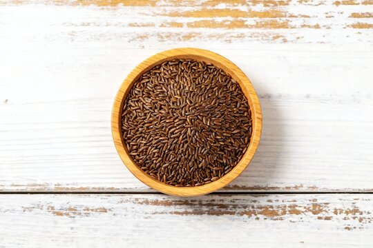 Brown flax seeds in wooden bowl on rustic white wood background