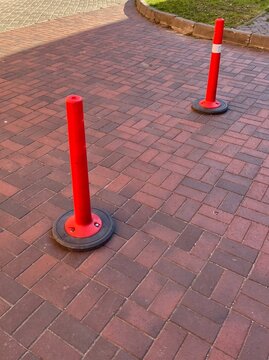 Two red delineator posts on brick pavement