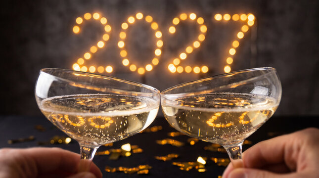Hands toasting champagne glasses with 2027 lights in festive background