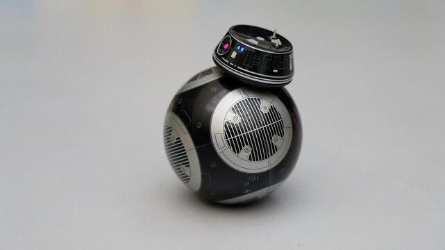Black spherical toy droid spinning on a gray background. Technology, pop culture, fiction and robotic concept.