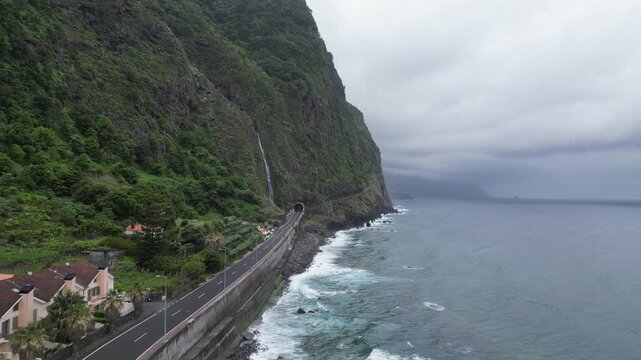 Aerial push-in along coastal highway towards Agua d'Alto waterfall and tunnel in Madeira