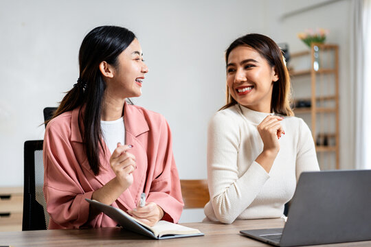 Two women are sitting at a table with a laptop and a notebook