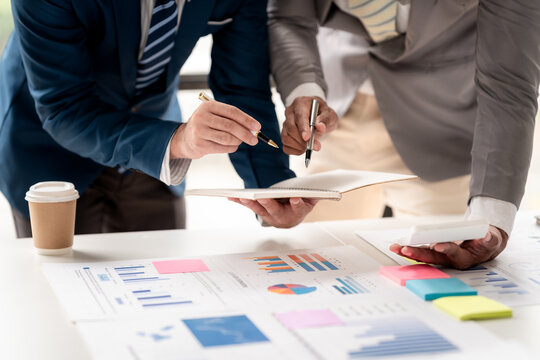 Two men are looking at a table with a lot of papers and a calculator