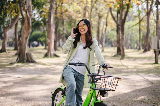 A woman is riding a green bicycle with a basket and talking on her cell phone