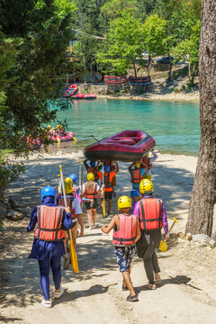 Group of individuals carrying a raft towards the Koprucay River in Antalya, Turkey, wearing helmets and life jackets, preparing for a rafting adventure