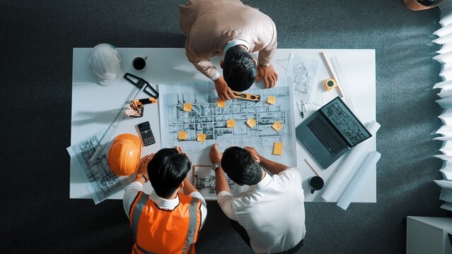 Top down aerial view of smart architect engineer team pointing and discussing about building construction. Group of diverse people working together to plan and design by using blueprint. Alimentation.