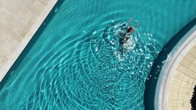 swimmer diving and swimming in a concrete poolside setting with a top-down perspective and active and dynamic mood, blue and green water, sports and recreation context.