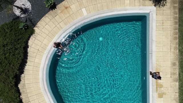 dynamic swimmer diving into a pool surrounded by green plants and brick wall, summer activities in blue water with clean background and vivid colors, sports and recreation.