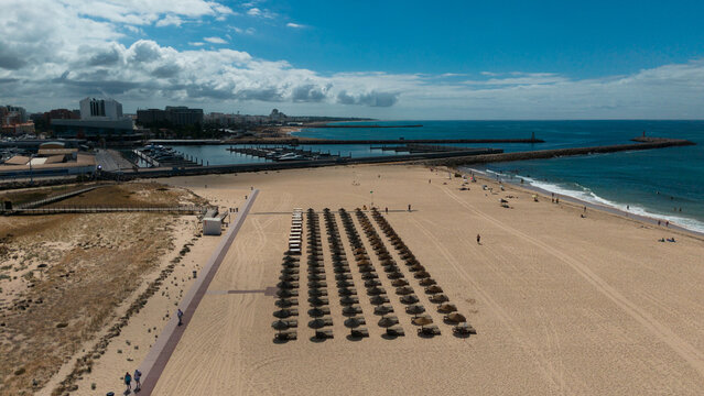 Aerial view of the luxury Falesia beach in Vilamoura. With sunbathing tourists on sun beds. Marina port with yachts, in the background.