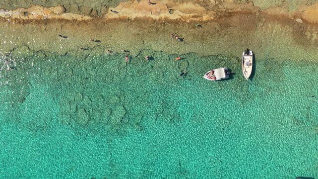 Overhead aerial drone view of swimmers in the crystal-clear turquoise shallows along the rocky shore of Gramvousa island, Gramvousa, Greece