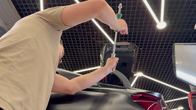 Professional car repair technician using a PDR slide hammer and a hook tool for paintless dent removal process on a vehicle body inside a detailing studio.
