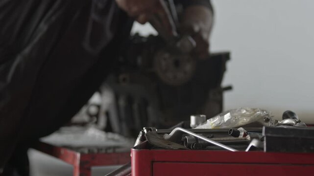 Mechanic assembling a crankshaft into an engine block with mechanical tools in a red toolbox in the foreground. Perfect for auto service and workshop concepts.