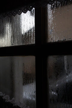 Silhouetted wooden window frame with heavy condensation and water droplets, vertical shot