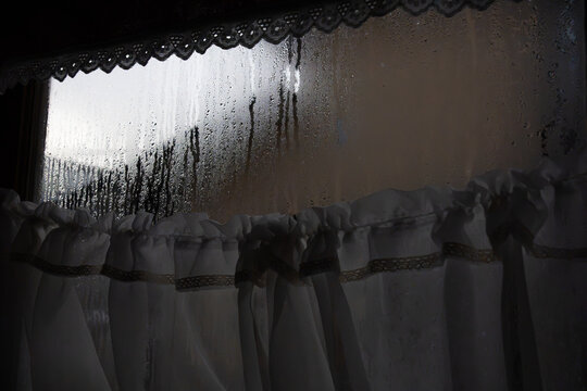 Heavy condensation and water droplets on a window glass pane with curtains, horizontal shot