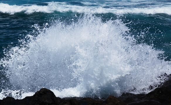 Powerful sea wave crashing against dark coastal rocks with explosive foam splash