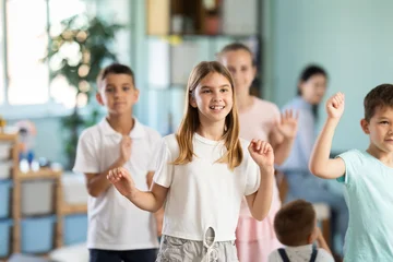 Children actively jump and dance during music lesson, teacher accompanies on piano in kindergarten, music lesson... © JackF