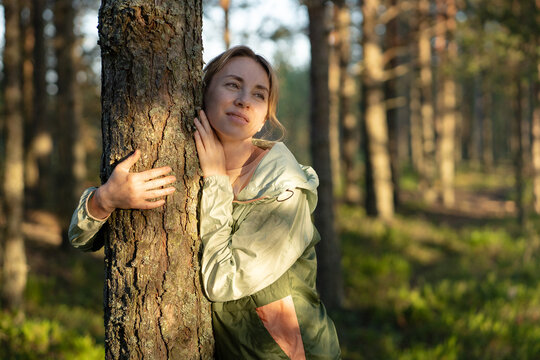 Smiling calm woman nature lover hugging tree in forest while enjoying forest bathing and relaxation, positive female embracing tree trunk, showing gratitude to nature, relieving stress, finding peace.