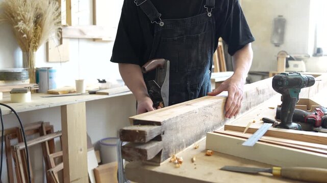 Handmade restoration of old items in workshop, man crafter using hand plane tool for shaping board with installed patch, carefully checking surface for roughness, handcraft and carpentry workspace.