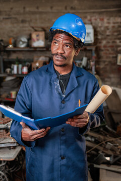African architect stands in a workshop looking at blueprints