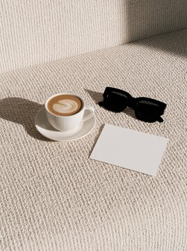 Blank card next to latte and black chic sunglasses on textured sofa surface