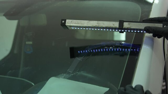 Mechanic cures resin inside windshield crack using lighting equipment 4k clip. Windshield UV Resin Curing. Windshield repair. Automotive technician holds ultraviolet lamp over broken car glass