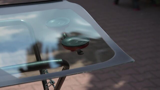 New transparent car glass awaits outdoor installation 4k video. Mobile Windshield Replacement Concept. Red vacuum lifter secures new car glass on outdoor repair stand