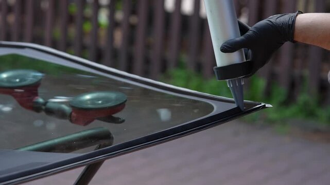 Applying urethane adhesive to a new windshield on a glass stand 4k video. Mechanic using a caulking gun to apply urethane to a new windshield